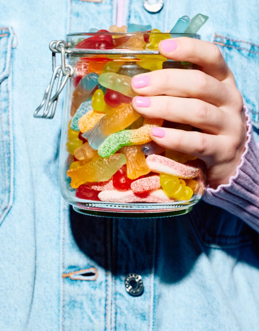 A hand holding a glass jar filled with gummies.